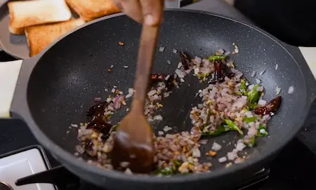 Spicy masala base with garlic, chillies, and curry leaves cooking in oil.