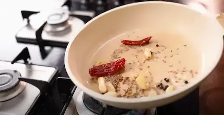 Sautéing jeera, black pepper, red chilies, garlic, and ginger for the masala base of Peanuts Ki Sabji.