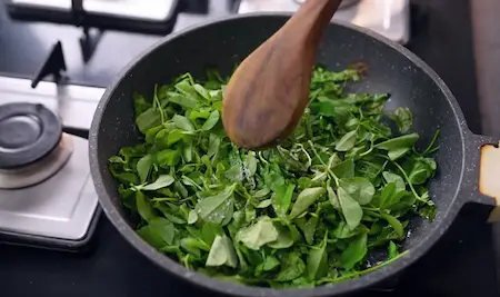 Sautéing methi leaves with oil and salt