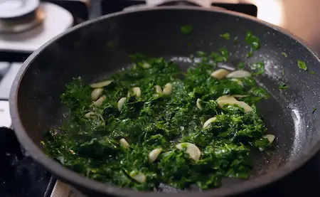 Sautéed garlic and cooked methi in a pan.