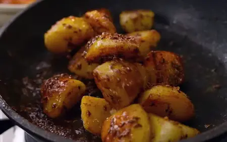 Potatoes being sautéed in a pan with cumin seeds