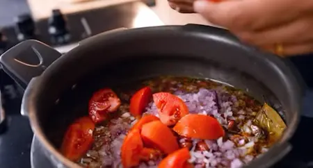 Adding soaked rajma and tomatoes to the pressure cooker