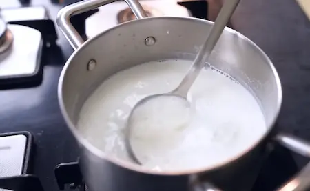 pouring and heating milk in a pan for homemade dahi