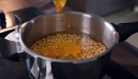 Adding boiled white vatana to masala for ghugni