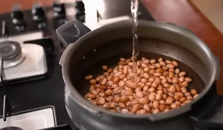 Pressure cooking peanuts in a cooker until tender for Peanuts Ki Sabji preparation.