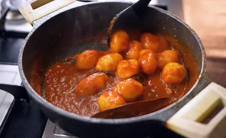 Cooking baby potatoes in masala for dum aloo in Aloo Dum Muri Ghugni